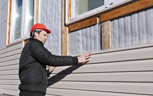 A worker installs panels beige siding on the facade